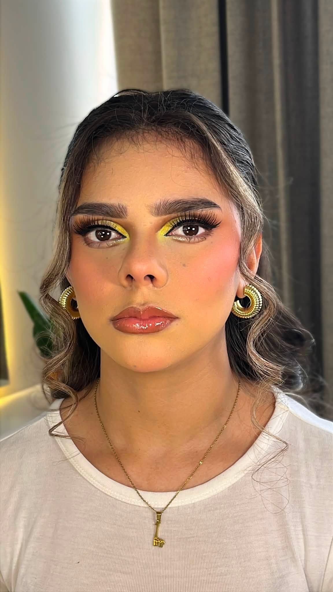 Maquillaje con acentos amarillos en el lagrimal, labios brillantes y cabello recogido