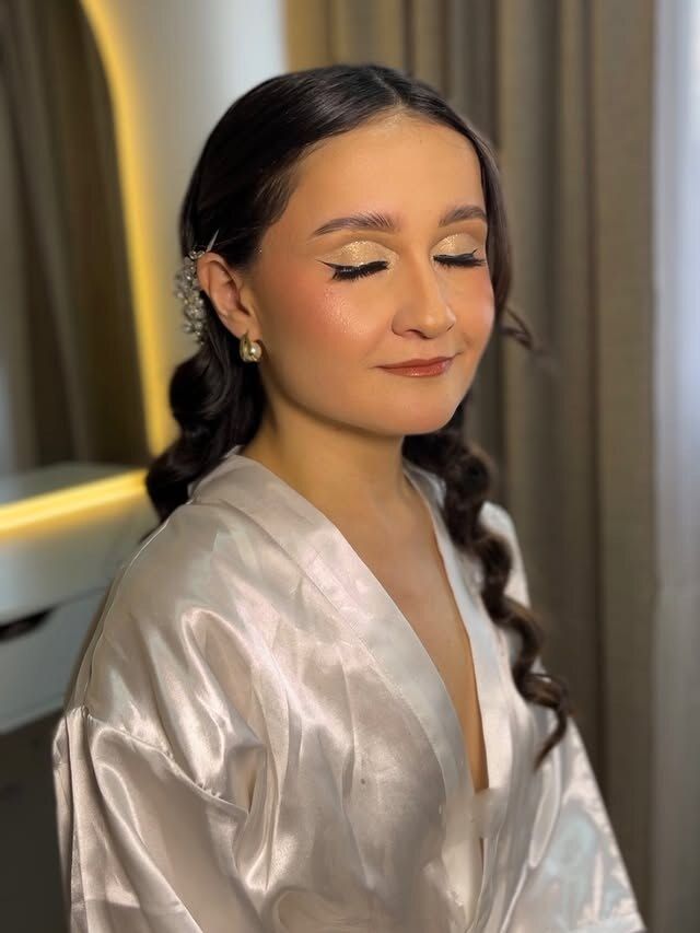 Novia con ojos cerrados, maquillaje cálido y bata satinada clara