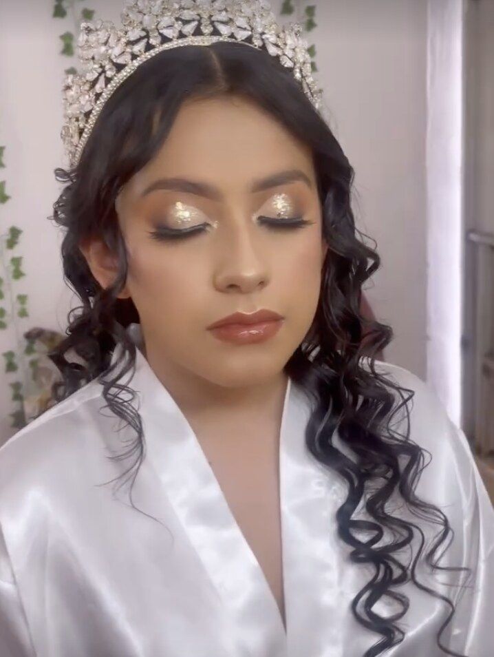 Quinceañera con corona de cristales, sombras doradas con brillo y labios nude